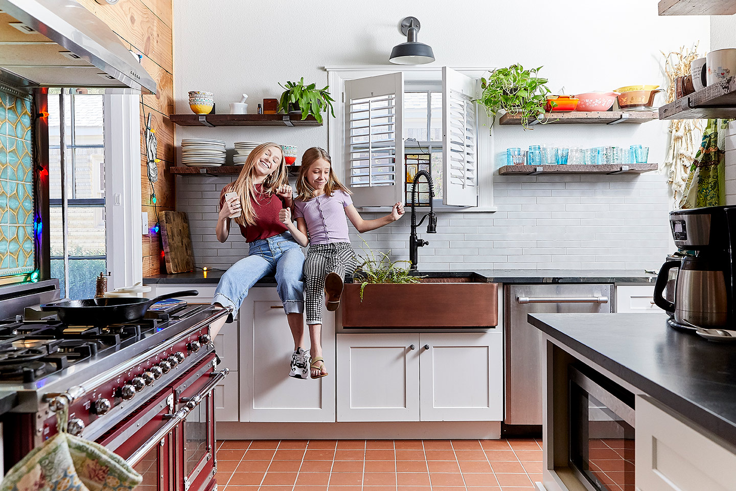 Indoor lifestyle photograph of two tweens dancing to music on the kitchen counter.