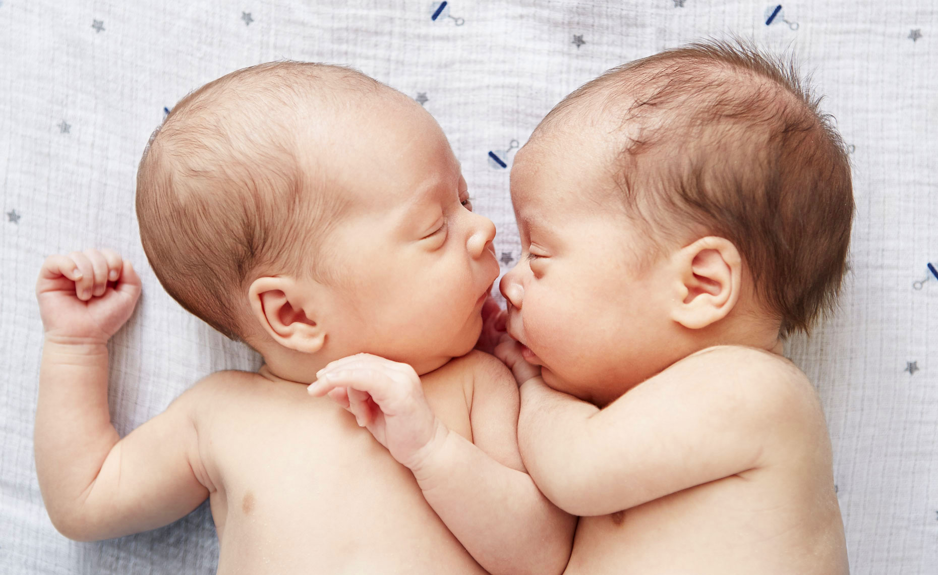 Indoor lifestyle photograph of two newborn babies laying on a bed together.