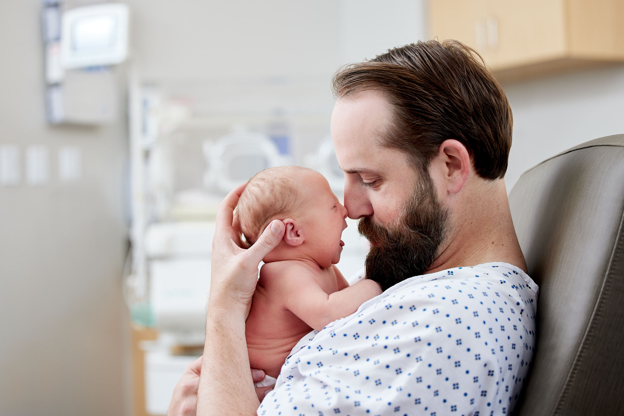 Indoor medical photograph of a new dad holding his newborn child in the hosptial.
