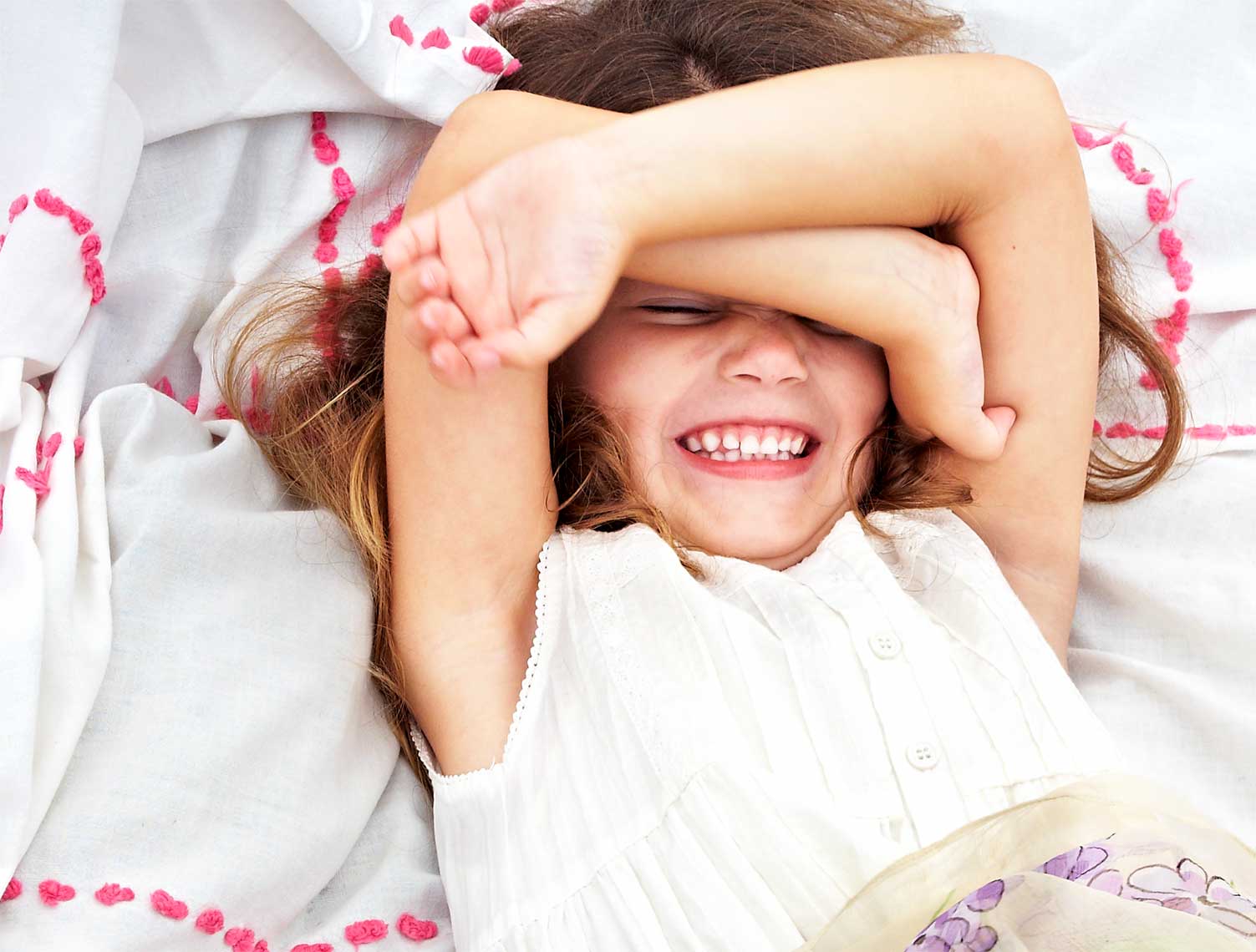Outdoor lifestyle photograph of a young girl laying on a blanket covering her face while smiling.